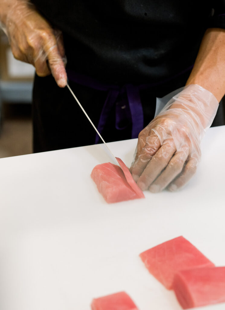 A worker hand cutting raw tuna for sushi